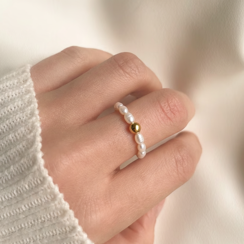 Perlenring aus kleinen Süßwasserperlen mit goldener Kugel auf der Hand