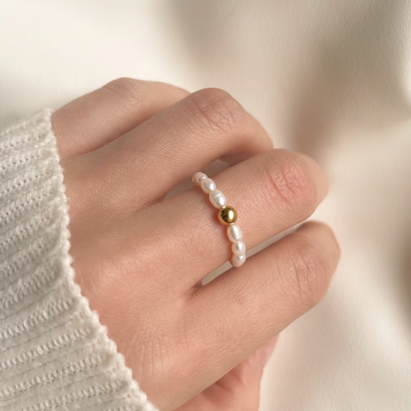 Perlenring aus kleinen Süßwasserperlen mit goldener Kugel auf der Hand